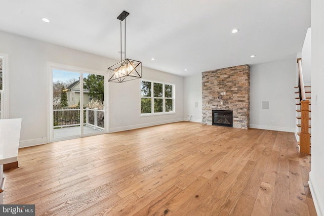 unfurnished living room with light wood-type flooring, a fireplace, and an inviting chandelier