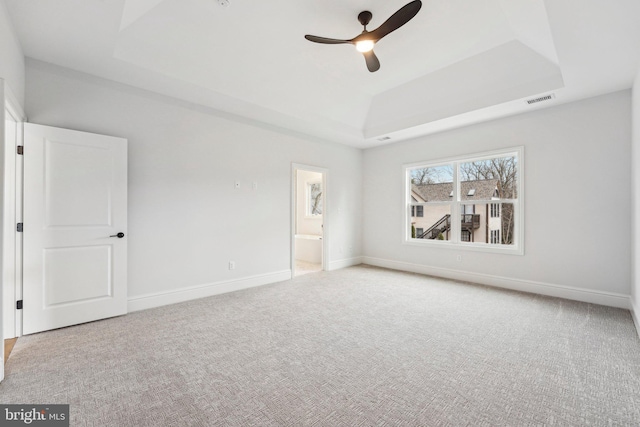 carpeted spare room with a raised ceiling and ceiling fan