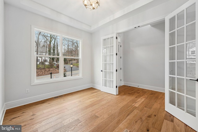 unfurnished room with a tray ceiling, a chandelier, french doors, and light hardwood / wood-style floors