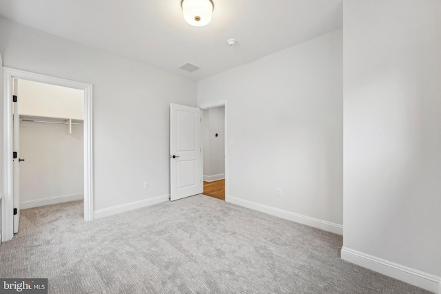 unfurnished bedroom featuring light colored carpet, a walk in closet, and a closet