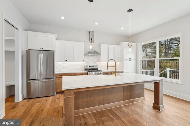 kitchen with appliances with stainless steel finishes, sink, wall chimney range hood, white cabinetry, and an island with sink