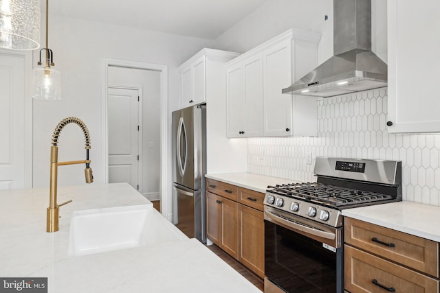 kitchen with pendant lighting, wall chimney range hood, decorative backsplash, appliances with stainless steel finishes, and white cabinetry