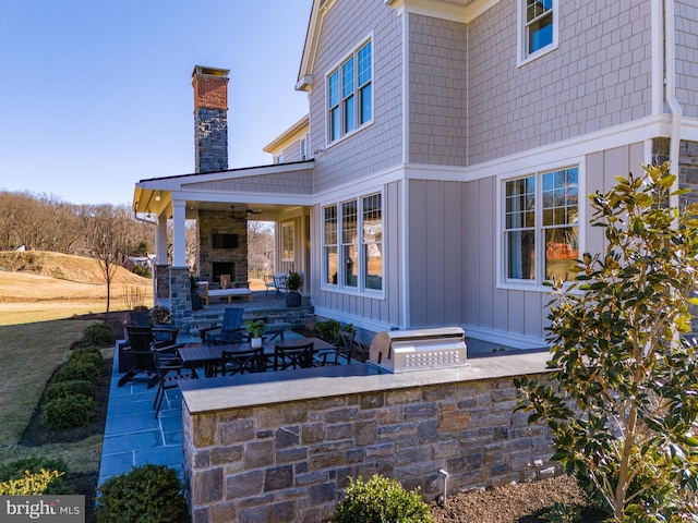 view of patio featuring ceiling fan, an outdoor stone fireplace, and exterior kitchen