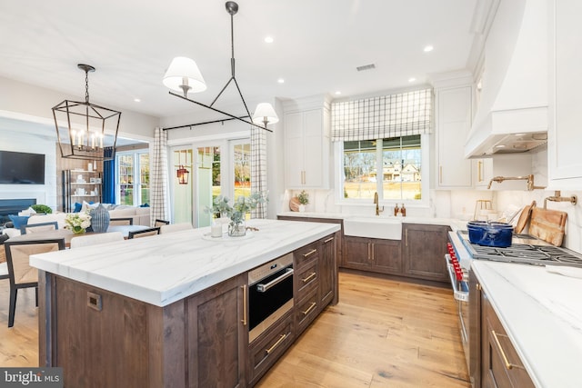 kitchen featuring custom exhaust hood, sink, stainless steel range, a kitchen island, and white cabinetry