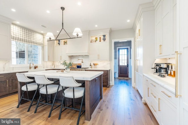 kitchen with a kitchen bar, light wood-type flooring, white cabinets, a kitchen island, and hanging light fixtures