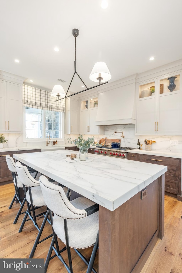 kitchen with a center island, light hardwood / wood-style floors, decorative light fixtures, white cabinets, and custom range hood