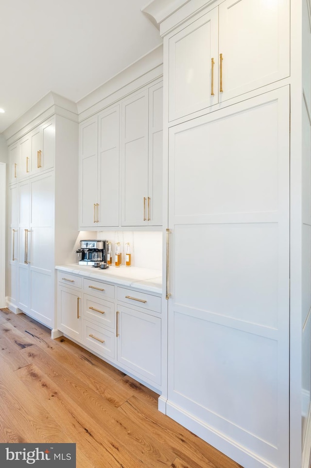 bar with white cabinets and light wood-type flooring