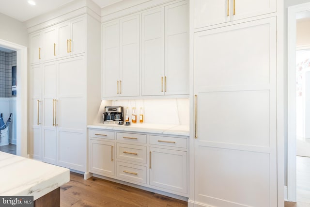 bar with light stone countertops, white cabinets, and light hardwood / wood-style floors