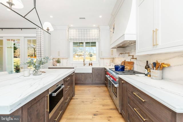 kitchen featuring white cabinetry, hanging light fixtures, range with two ovens, and custom exhaust hood