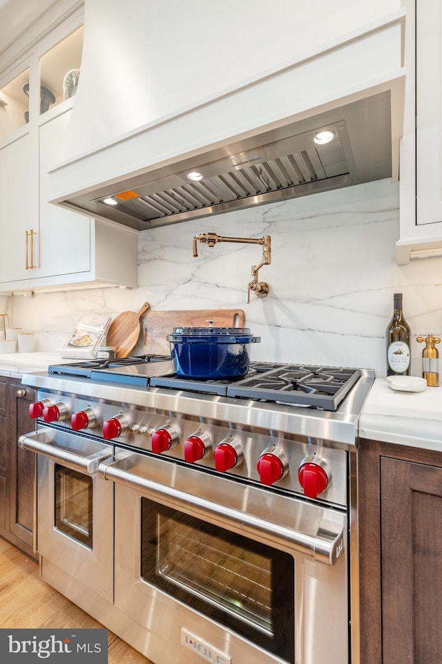 kitchen featuring custom range hood, backsplash, white cabinetry, and range with two ovens