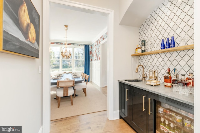 interior space with beverage cooler, wet bar, crown molding, a chandelier, and light hardwood / wood-style floors