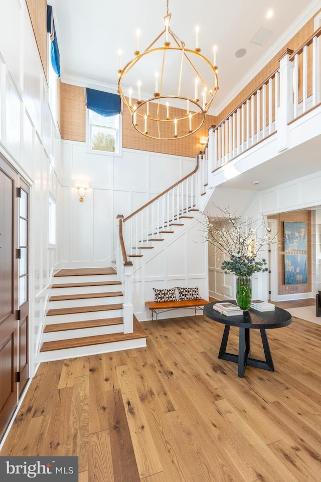 entryway featuring light hardwood / wood-style flooring, a towering ceiling, and ornamental molding