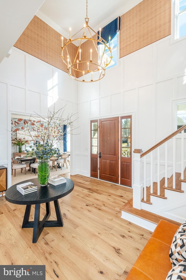 entryway featuring wood-type flooring, ornamental molding, a high ceiling, and a chandelier