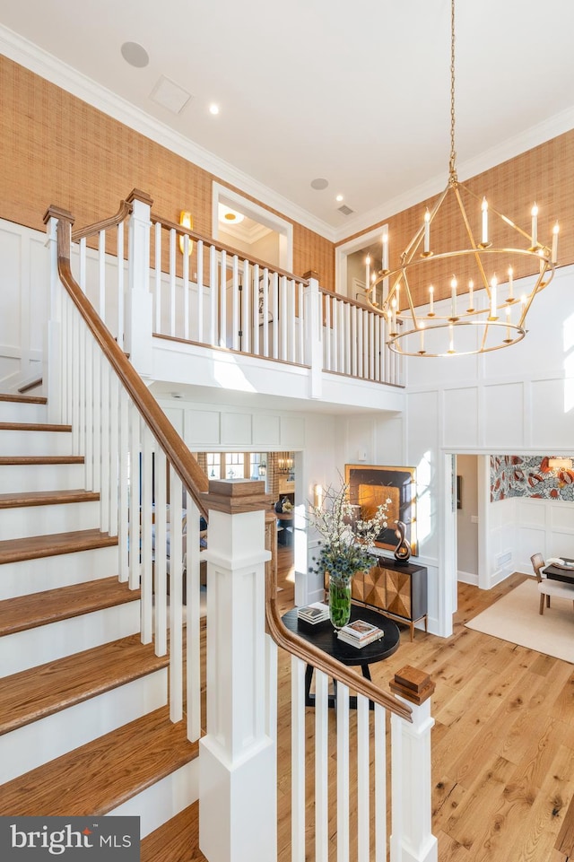 stairs with ornamental molding, a notable chandelier, and hardwood / wood-style flooring