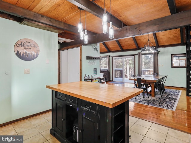 kitchen featuring light tile patterned flooring, beamed ceiling, hanging light fixtures, butcher block countertops, and a kitchen island