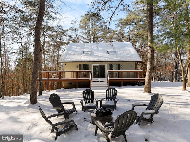 snow covered rear of property with a wooden deck and an outdoor fire pit