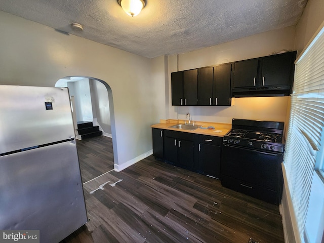 kitchen with a textured ceiling, sink, black gas stove, dark hardwood / wood-style floors, and stainless steel refrigerator