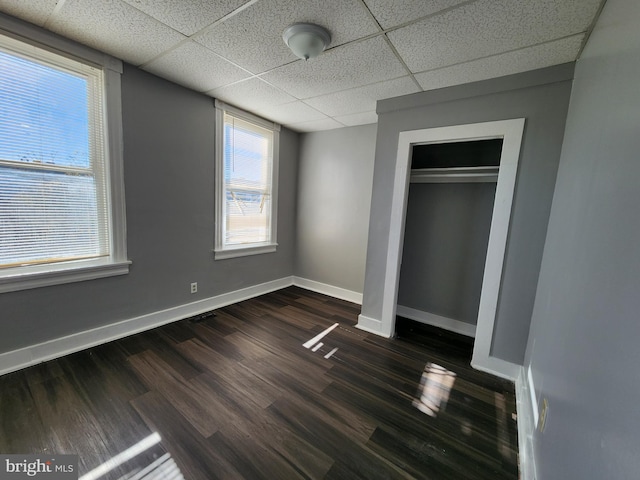 unfurnished bedroom featuring a closet, dark wood-type flooring, and a drop ceiling