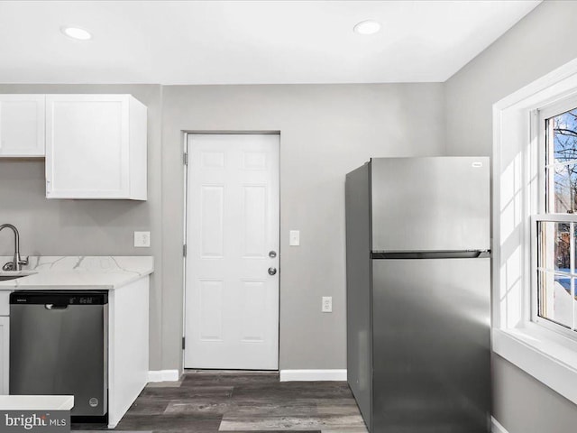 kitchen with light stone countertops, appliances with stainless steel finishes, dark wood-type flooring, sink, and white cabinetry