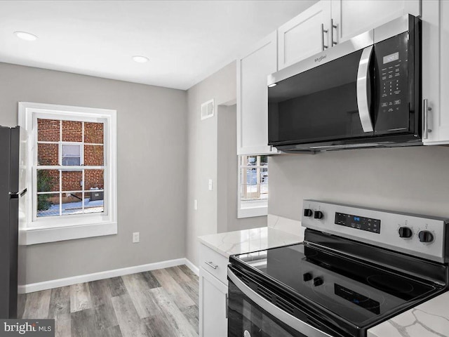 kitchen with light stone counters, white cabinets, light wood-type flooring, and appliances with stainless steel finishes