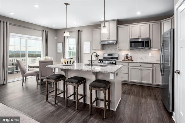 kitchen featuring sink, dark wood-type flooring, stainless steel appliances, an island with sink, and decorative light fixtures