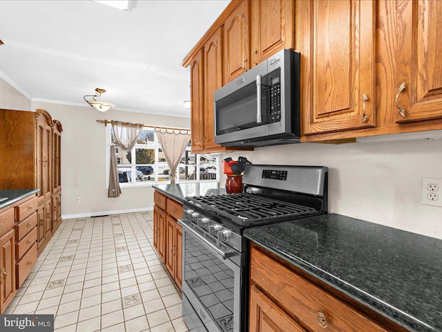 kitchen with dark stone counters, stainless steel appliances, ornamental molding, and light tile patterned flooring