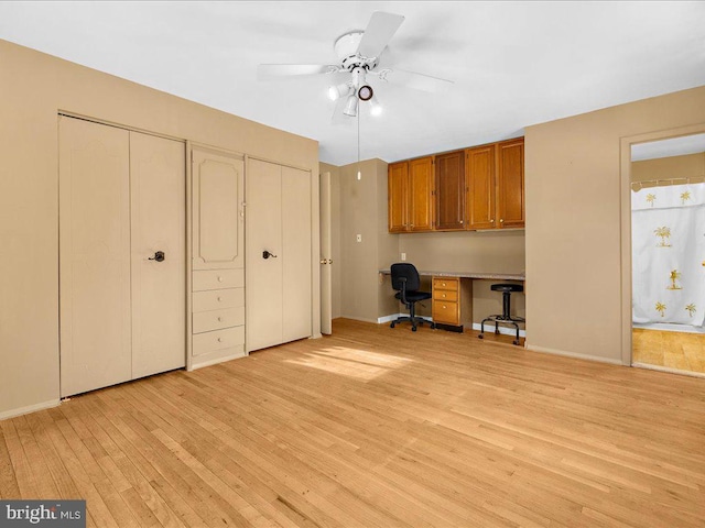 unfurnished office featuring built in desk, light hardwood / wood-style floors, and ceiling fan