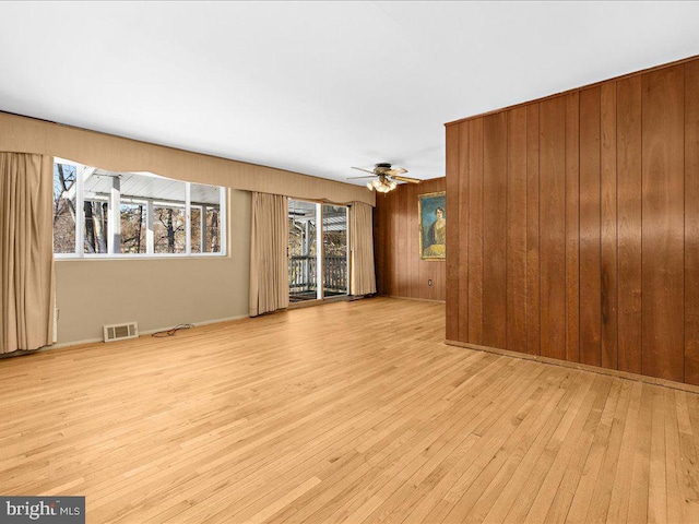 spare room featuring light hardwood / wood-style flooring, ceiling fan, and wooden walls