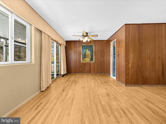 spare room featuring ceiling fan, light hardwood / wood-style floors, plenty of natural light, and wood walls