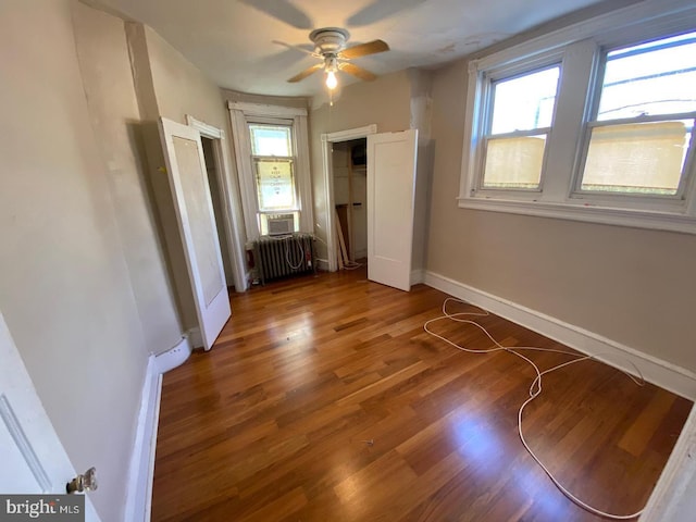 unfurnished bedroom featuring radiator, ceiling fan, wood-type flooring, and multiple windows