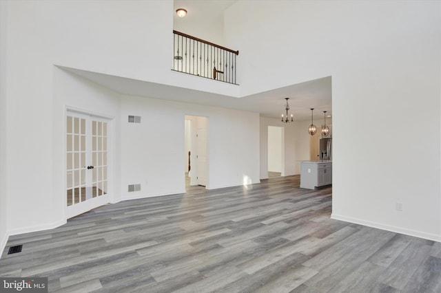 unfurnished living room with a high ceiling, light wood-type flooring, french doors, and a notable chandelier