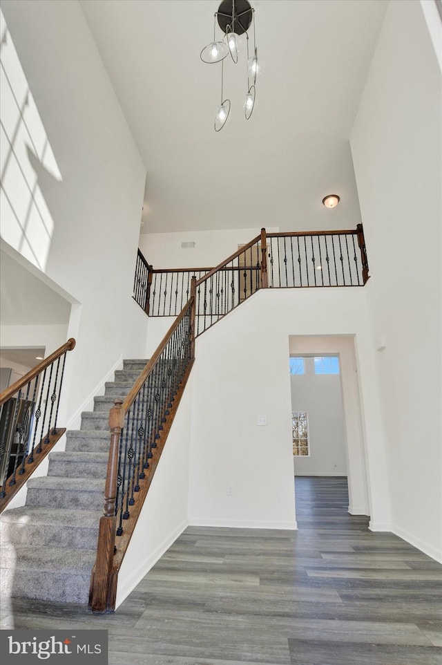 stairs with hardwood / wood-style floors, a towering ceiling, and a notable chandelier