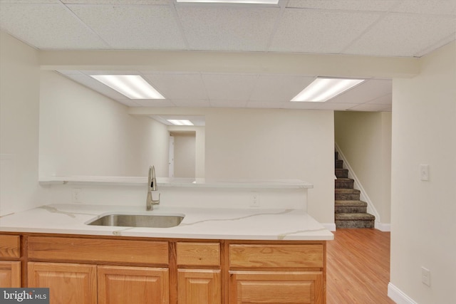 kitchen featuring light stone counters, sink, a drop ceiling, and light wood-type flooring