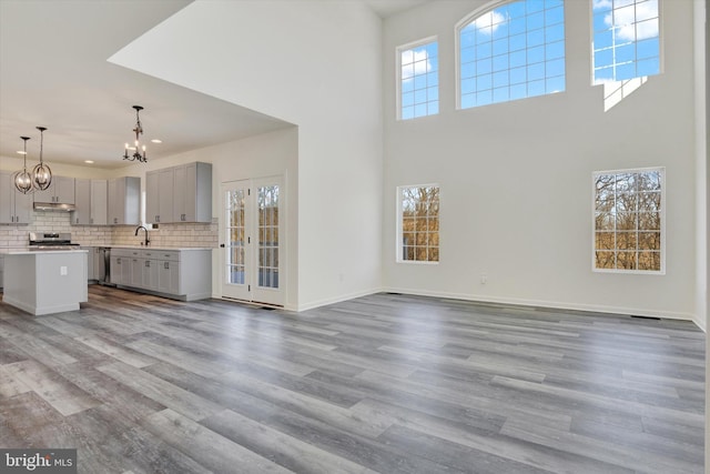 unfurnished living room featuring sink, a healthy amount of sunlight, a high ceiling, an inviting chandelier, and light wood-type flooring