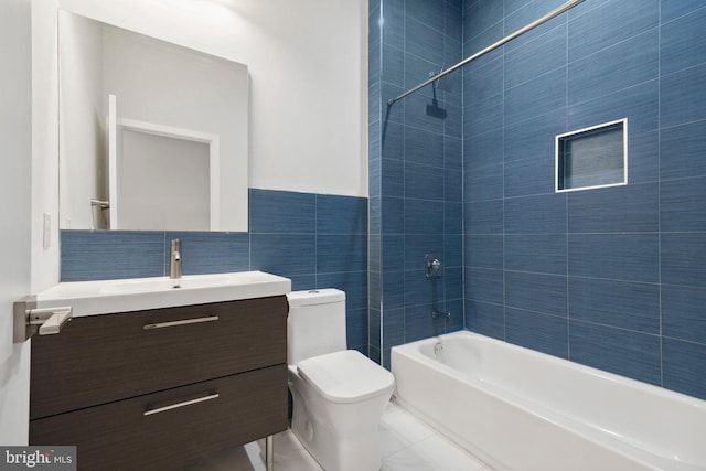 full bathroom featuring tiled shower / bath, vanity, toilet, and tile walls