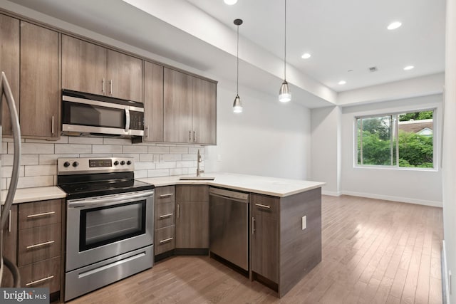 kitchen featuring sink, stainless steel appliances, kitchen peninsula, decorative light fixtures, and decorative backsplash