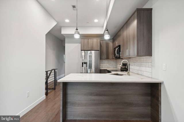 kitchen featuring light stone countertops, stainless steel appliances, backsplash, kitchen peninsula, and decorative light fixtures