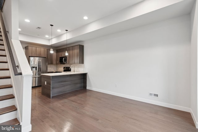 kitchen featuring backsplash, kitchen peninsula, wood-type flooring, decorative light fixtures, and appliances with stainless steel finishes