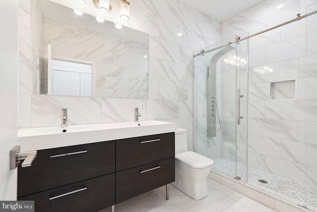 bathroom with a shower with door, vanity, tile walls, and toilet