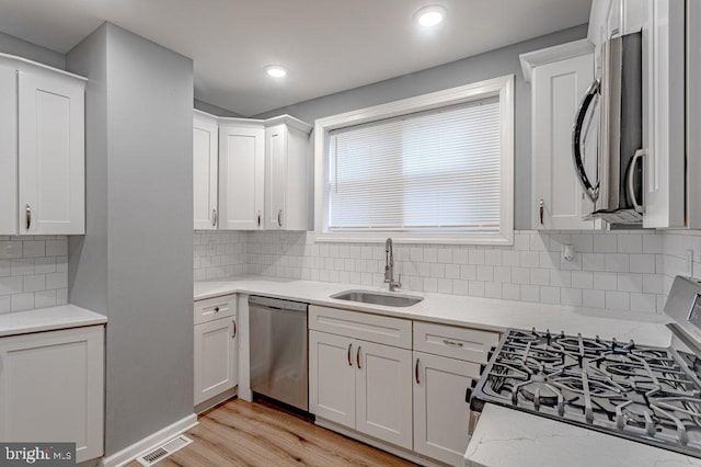 kitchen featuring decorative backsplash, light wood-type flooring, stainless steel appliances, sink, and white cabinets