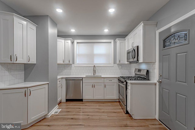 kitchen with sink, light hardwood / wood-style floors, decorative backsplash, white cabinets, and appliances with stainless steel finishes