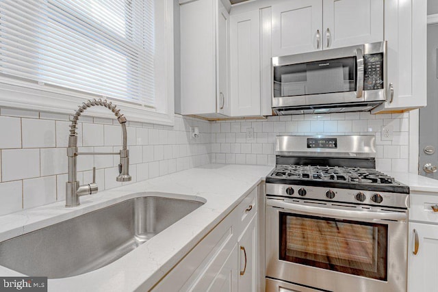 kitchen with white cabinets, stainless steel appliances, light stone countertops, and sink