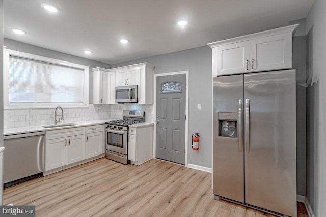 kitchen featuring sink, stainless steel appliances, light hardwood / wood-style flooring, backsplash, and white cabinets