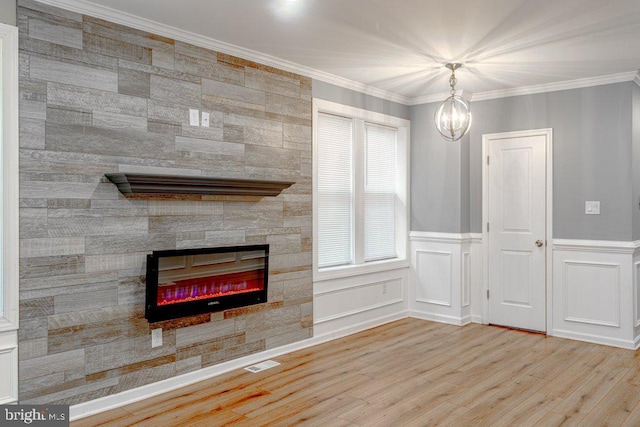 unfurnished living room with plenty of natural light, light hardwood / wood-style flooring, ornamental molding, a fireplace, and a notable chandelier