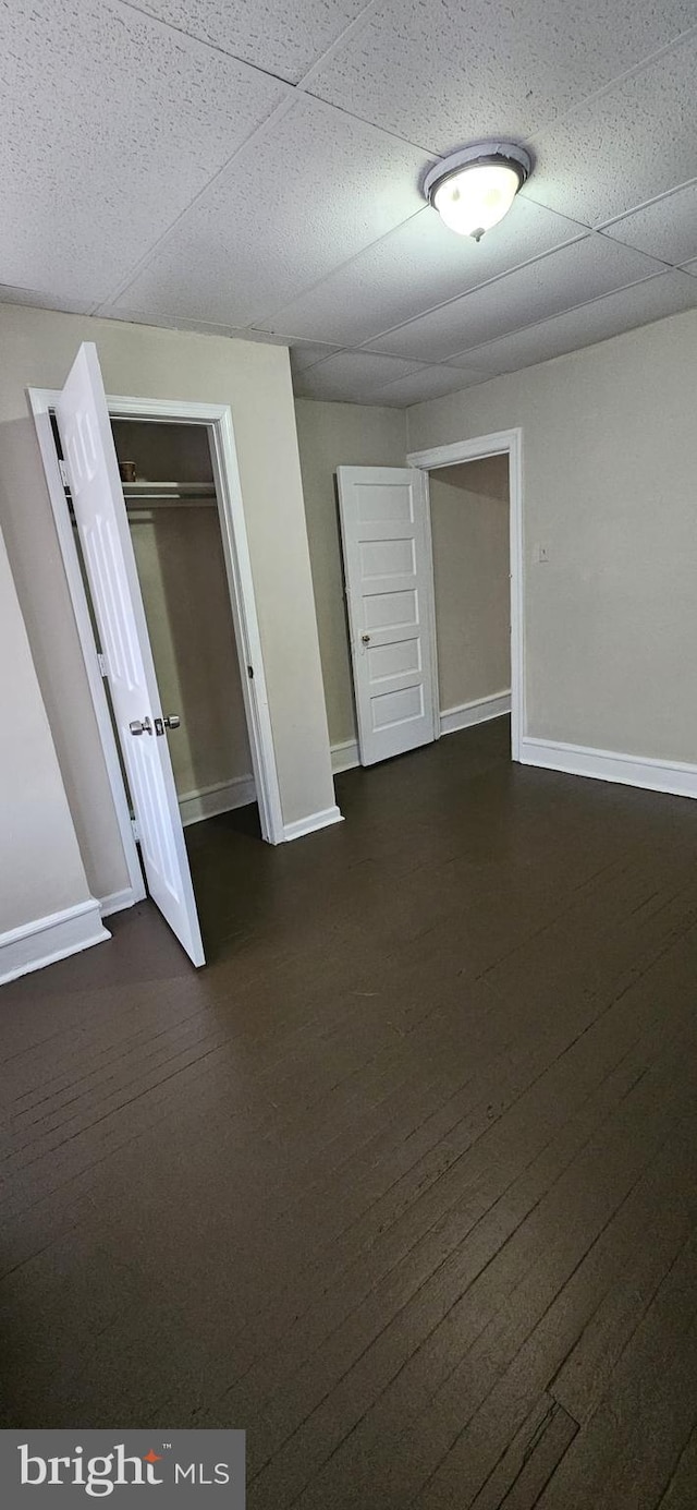 unfurnished bedroom with a closet, dark wood-type flooring, and a drop ceiling