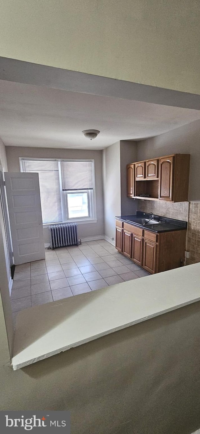 kitchen with sink, light tile patterned flooring, backsplash, and radiator heating unit