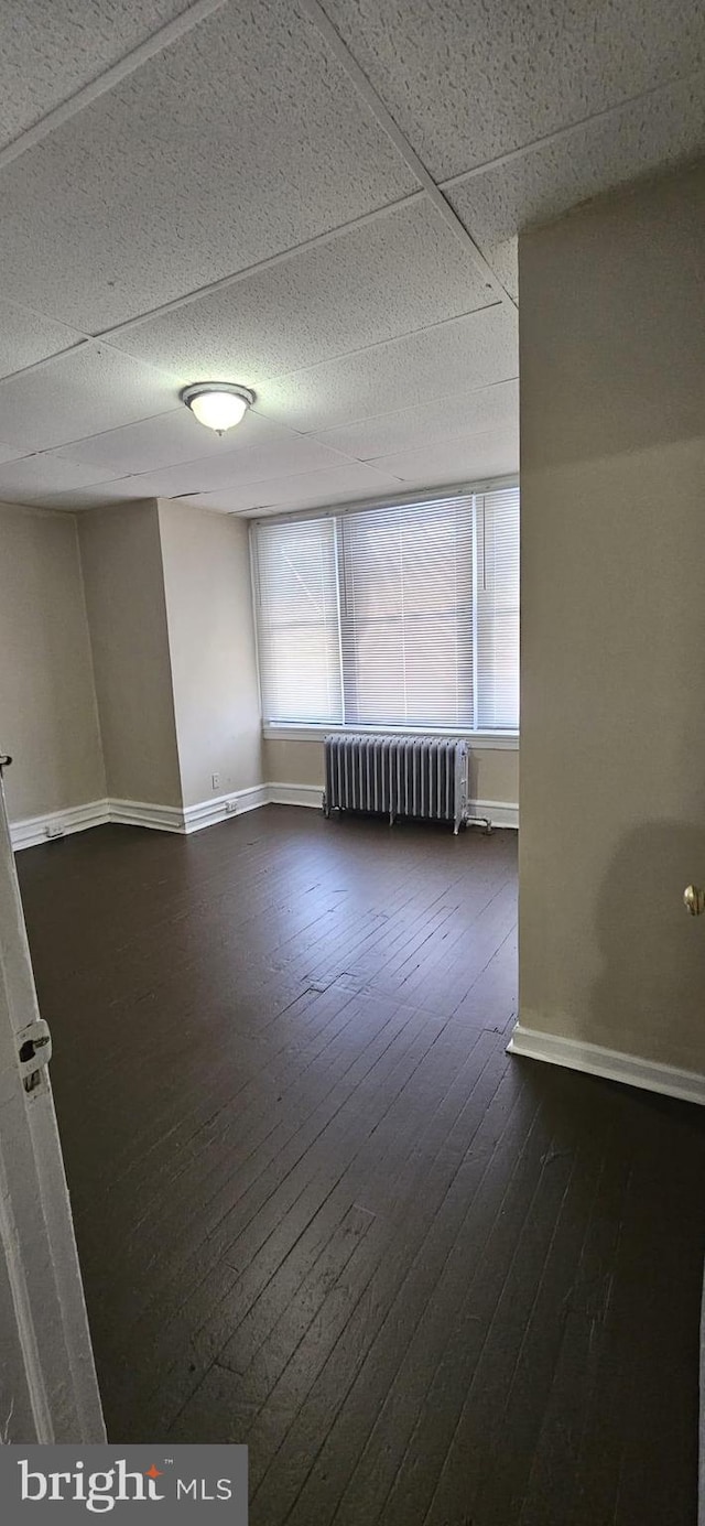 empty room featuring dark wood-type flooring, a paneled ceiling, and radiator