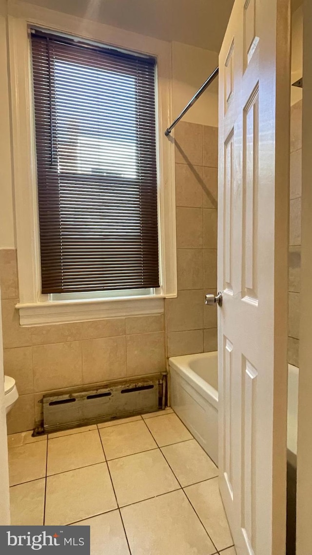 bathroom featuring tile patterned flooring, tile walls, toilet, and tiled shower / bath