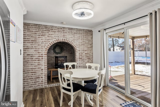 dining room featuring wood-type flooring, a brick fireplace, crown molding, and brick wall