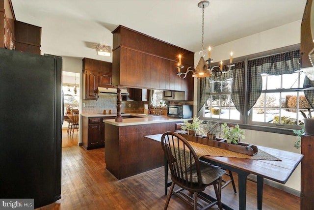 kitchen with decorative backsplash, dark hardwood / wood-style flooring, dark brown cabinets, black appliances, and a chandelier